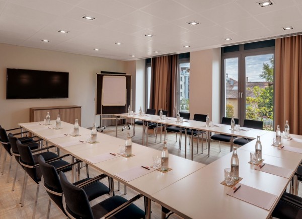 Lichtdurchfluteter Tagungsraum mit Tischen in U-Form, Flachbildschirm und Whiteboard